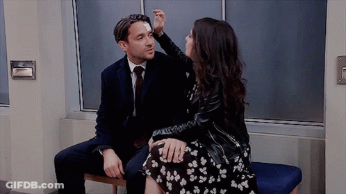 A Man And A Woman Are Sitting Next To Each Other On A Bench . The Woman Is Touching The Man 'S Face . GIF