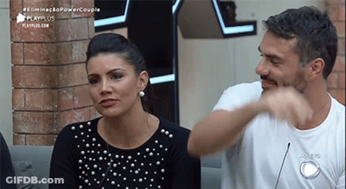 A Man And A Woman Are Sitting Next To Each Other On A Couch And The Man Is Pointing At The Woman . GIF