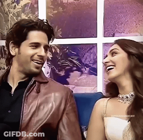 A Man And A Woman Are Sitting Next To Each Other On A Couch Laughing . GIF