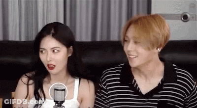 A Man And A Woman Are Sitting Next To Each Other On A Couch . The Man Is Wearing A Striped Shirt . GIF