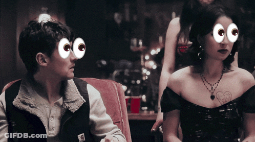 A Man And A Woman Are Sitting Next To Each Other With Cartoon Eyes On Their Faces GIF