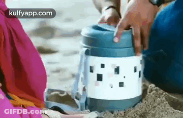 A Man And A Woman Are Sitting On A Beach Holding A Thermos . GIF