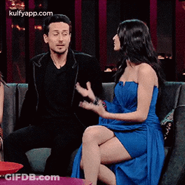 A Man And A Woman Are Sitting On A Couch And Talking . The Woman Is Wearing A Blue Dress . GIF
