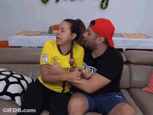 A Man And A Woman Are Sitting On A Couch And The Woman Is Wearing A Yellow Shirt That Says Barça GIF
