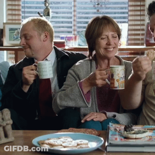 A Man And A Woman Are Sitting On A Couch Drinking Coffee And Smiling GIF