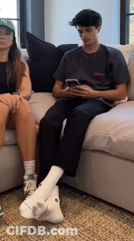 A Man And A Woman Are Sitting On A Couch Looking At Their Cell Phones GIF