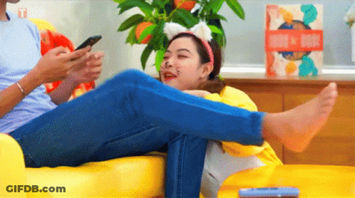 A Man And A Woman Are Sitting On A Couch Looking At Their Phones . The Woman Is Wearing Cat Ears . GIF