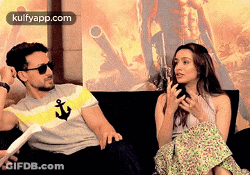 A Man And A Woman Are Sitting On A Couch Talking . GIF