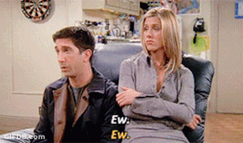 A Man And A Woman Are Sitting On A Couch With A Dart Board In The Background GIF