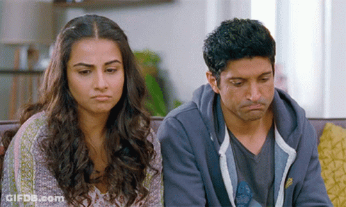 A Man And A Woman Are Sitting On A Couch With Their Faces Turned Towards The Camera GIF