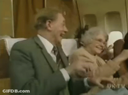 A Man And A Woman Are Sitting On A Plane Laughing And Hugging Each Other . GIF