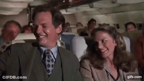 A Man And A Woman Are Sitting On A Plane Laughing And Smiling . GIF