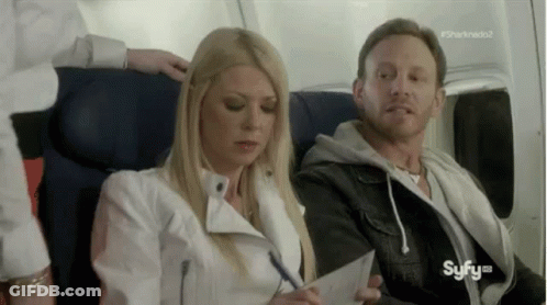 A Man And A Woman Are Sitting On A Plane . The Woman Is Writing On A Piece Of Paper . GIF
