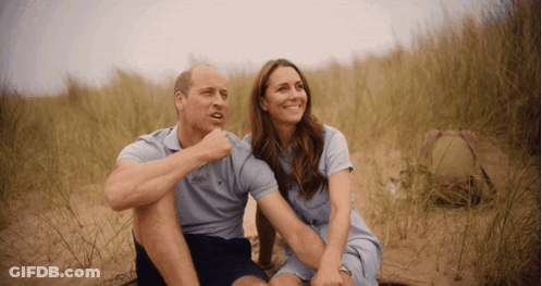A Man And A Woman Are Sitting On A Sandy Field GIF