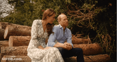 A Man And A Woman Are Sitting On Logs Holding Hands GIF
