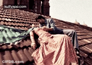 A Man And A Woman Are Sitting On Top Of A Roof . GIF