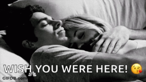 A Man And A Woman Are Sleeping In A Bed With The Words `` Wish You Were Here '' Written Above Them . GIF