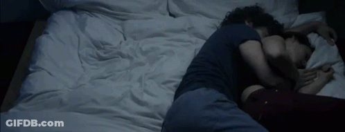 A Man And A Woman Are Sleeping On A Bed With White Sheets GIF