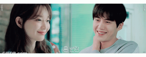 A Man And A Woman Are Smiling And Looking At Each Other In A Room . GIF