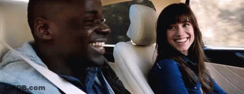 A Man And A Woman Are Smiling In The Back Seat Of A Car . GIF