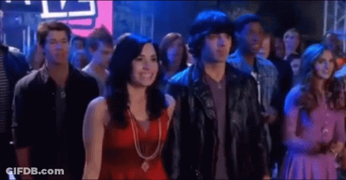 A Man And A Woman Are Standing In A Crowd Of People At A Party . GIF