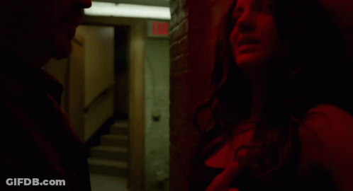 A Man And A Woman Are Standing In A Dark Room With A Red Exit Sign In The Background GIF
