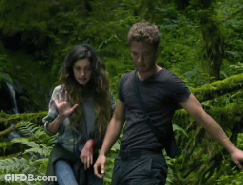 A Man And A Woman Are Standing In A Forest GIF