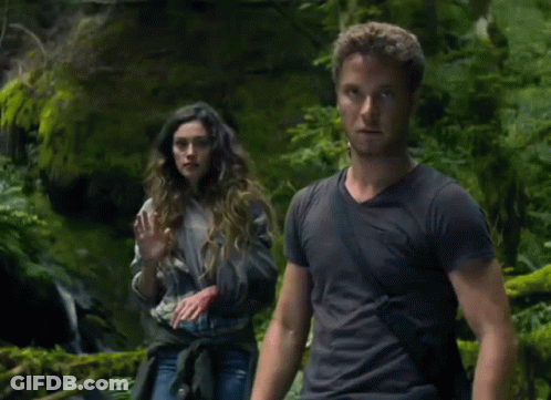 A Man And A Woman Are Standing In A Forest GIF