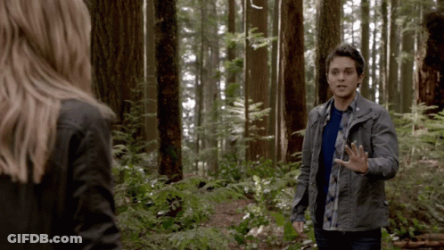 A Man And A Woman Are Standing In A Forest Talking To Each Other GIF