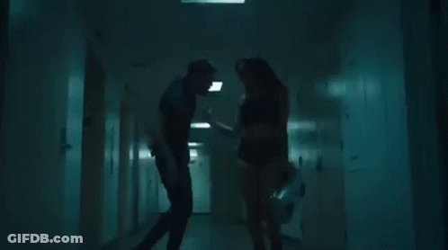 A Man And A Woman Are Standing In A Hallway . GIF