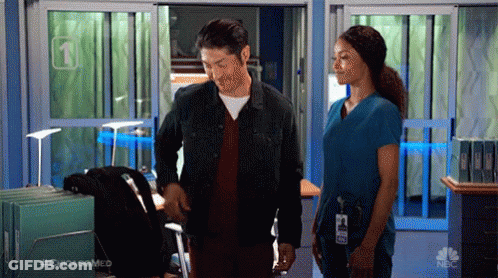 A Man And A Woman Are Standing In A Hospital Hallway . GIF
