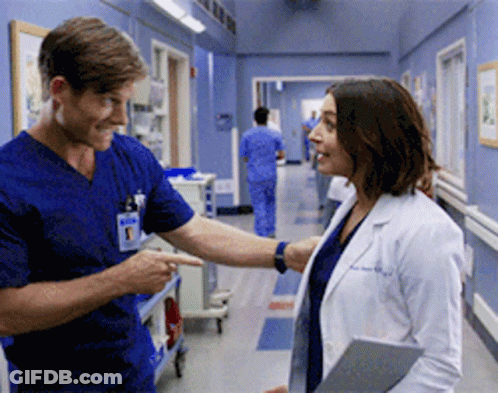 A Man And A Woman Are Standing In A Hospital Hallway GIF