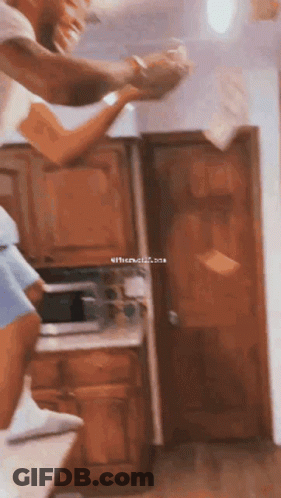 A Man And A Woman Are Standing In A Kitchen Holding Hands While The Woman Throws Papers In The Air . GIF
