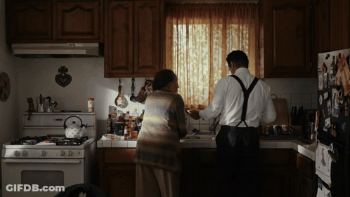 A Man And A Woman Are Standing In A Kitchen GIF