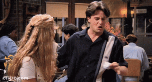 A Man And A Woman Are Standing In A Restaurant And The Man Is Wearing A Shirt That Says Hh GIF
