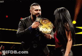 A Man And A Woman Are Standing In A Ring Holding A Championship Belt . GIF
