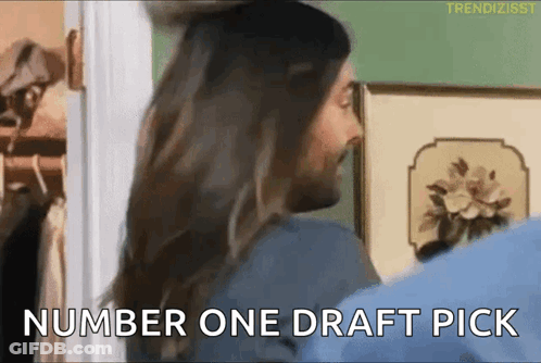 A Man And A Woman Are Standing In A Room And The Man Is Saying Number One Draft Pick GIF