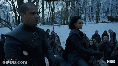 A Man And A Woman Are Standing In A Snowy Forest With The Word Got On The Bottom GIF