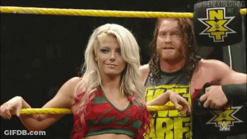 A Man And A Woman Are Standing In A Wrestling Ring Holding Yellow Ropes . GIF