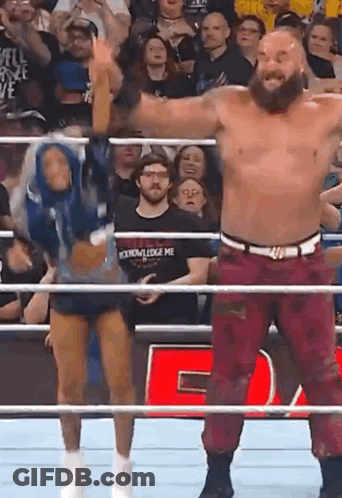 A Man And A Woman Are Standing In A Wrestling Ring With Their Arms In The Air . GIF