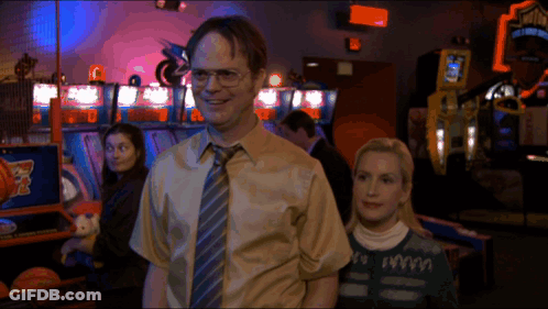 A Man And A Woman Are Standing In An Arcade With A Sign That Says ' Basketball ' On It GIF