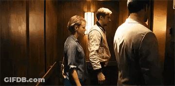 A Man And A Woman Are Standing In An Elevator With A Man Standing Behind Them . GIF