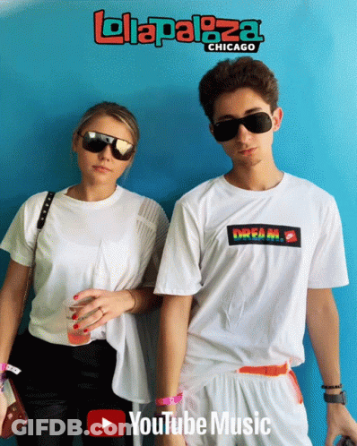 A Man And A Woman Are Standing In Front Of A Blue Wall That Says Lollapaloza Chicago On It GIF
