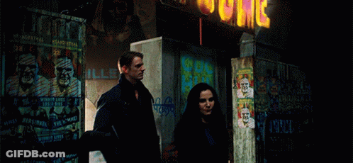 A Man And A Woman Are Standing In Front Of A Building With A Sign That Says ' Jc ' GIF
