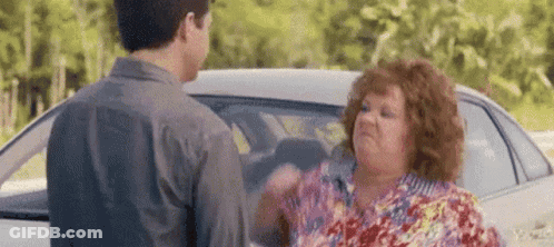A Man And A Woman Are Standing In Front Of A Car . GIF