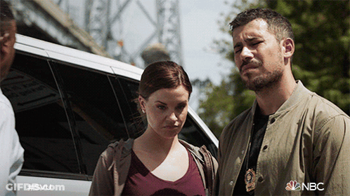 A Man And A Woman Are Standing In Front Of A Car With The Nbc Logo On The Bottom GIF