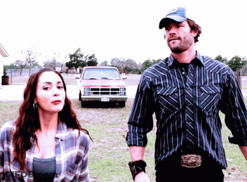 A Man And A Woman Are Standing In Front Of A Dodge Truck With A Texas License Plate GIF