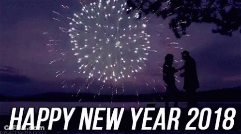 A Man And A Woman Are Standing In Front Of A Fireworks Display With The Words `` Happy New Year 2018 '' . GIF