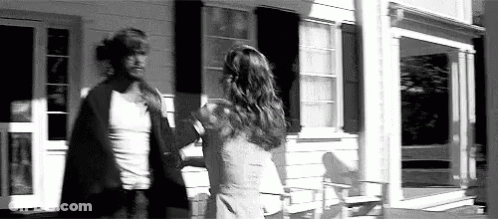 A Man And A Woman Are Standing In Front Of A House . GIF