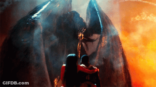 A Man And A Woman Are Standing In Front Of A Large Monster GIF